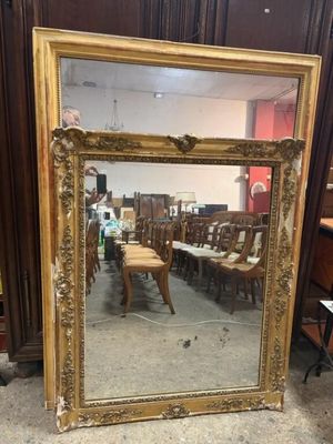 an antique gold framed mirror with a chair and a table in the background