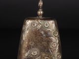 une vieille clochette en argent ornée d'un motif floral