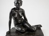 une sculpture noire représentant une femme assise sur un rocher