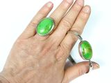 a woman ' s hand holding a ring with a green stone on it
