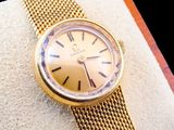 une montre en or montée sur un bracelet en or, posée sur un oreiller blanc