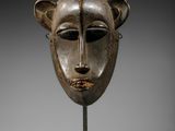 un masque en bois sur un support avec un fond noir