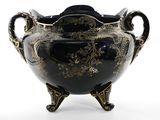 un vase noir et doré posé sur un socle, sur une surface blanche