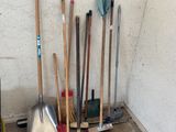 a pile of brooms and shovels in the corner of a room