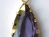 un gros plan d'un pendentif violet en forme de larme posé sur une surface blanche