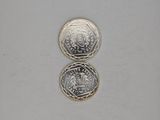 two silver coins sitting on top of each other on a white surface