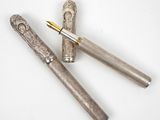 two silver pens sitting next to each other on top of a white surface
