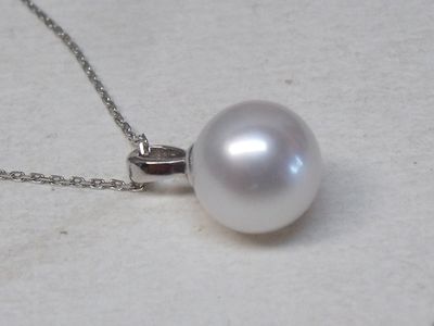 une perle blanche suspendue à une chaîne en argent sur un fond blanc