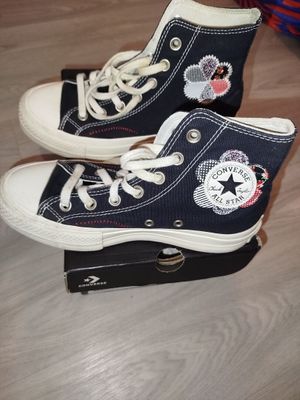 une paire de baskets Converse noires avec des lacets blancs, posée sur une boîte
