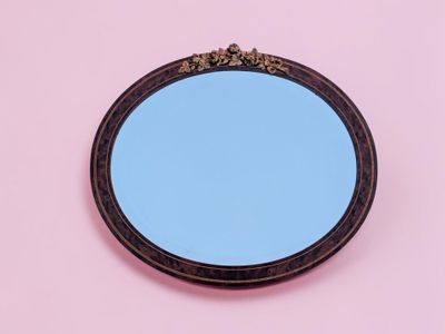 un gros plan sur un miroir posé sur une surface rose, avec un ciel bleu en arrière-plan