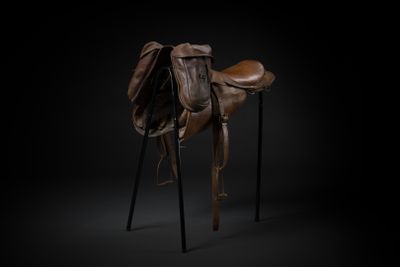 a brown horse saddle sitting on top of a wooden stand