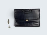 une mallette en cuir noir avec deux clés et un porte-clés, posée sur une surface blanche