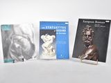 trois livres posés sur une table blanche, accompagnés d'une statue d'homme et d'une statue de femme