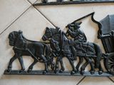 une sculpture métallique représentant une calèche tirée par des chevaux, avec des personnes à bord
