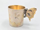 a gold cup with a butterfly on the side of it