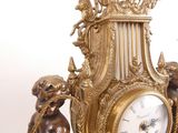 a gold clock with statues around it on a white surface