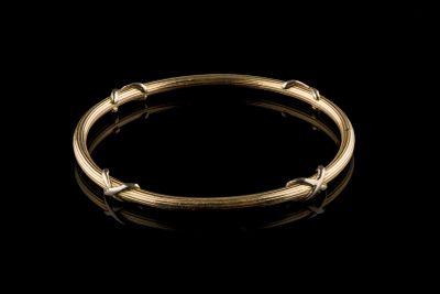 a gold bang bracelet with small beads on a black background