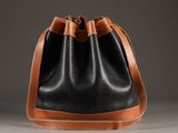 black and tan leather bucket bag on grey background