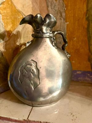 un vase en argent posé sur un sol carrelé, près d'un mur