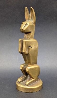 une statue en or représentant un lapin, posée sur un socle, sur un fond gris