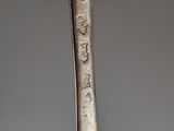 an old silver spoon with writing on it sitting on top of a table