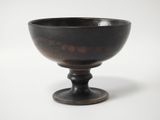 a black bowl on a pedestal on a white surface