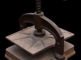 an old iron press with a wooden base on a black background
