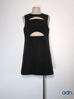 une robe noire ajourée posée sur un mannequin, devant un mur blanc