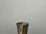 silver metal vase with holes in it on a gray surface