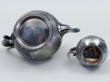 two silver teapots and a silver cup on a white surface