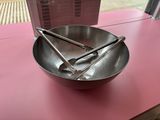 a metal bowl with spoons in it on a pink table