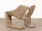 pair of tan leather lounge chairs on concrete floor with white wall