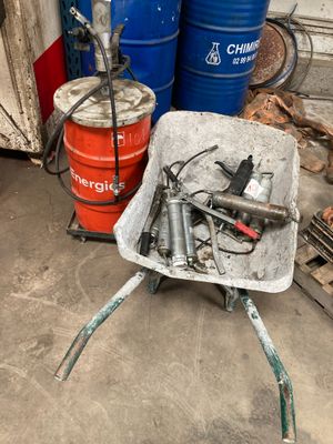 une brouette contenant tout un tas d'outils, à côté de quelques tonneaux