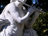 a statue of a woman playing a flute in front of trees