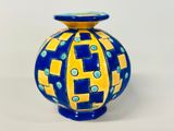 un vase bleu et jaune posé sur une surface blanche