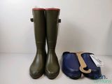 deux paires de bottes de pluie vertes et un étui bleu posés sur une surface blanche