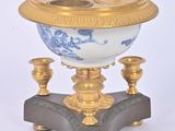une horloge dorée et bleue posée sur un socle, sur fond blanc