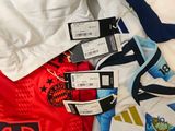 many different soccer shirts on a bed with tags on them
