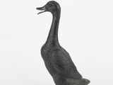 a small metal duck that is standing on a white surface