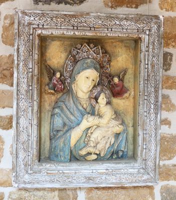 tableau représentant une femme tenant un bébé dans ses bras, encadré et accroché à un mur de pierre