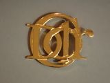 une broche en or sur laquelle figure la lettre « d »