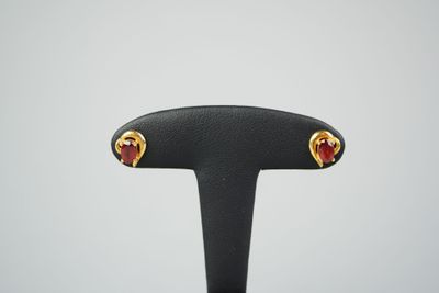 une paire de boucles d'oreilles en forme de cœur, dorées et rouges, posées sur un support noir