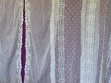 two white curtains with laces hanging on a wall