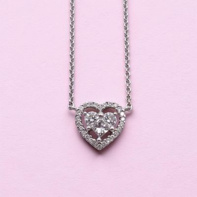 a close up of a heart shaped diamond necklace on a pink background