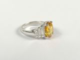 a close up of a yellow sapphire and diamond ring on a white surface