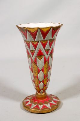un vase rouge et doré posé sur une surface blanche