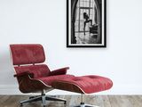 a black and white photo of a woman sitting on a red chair in front of a window