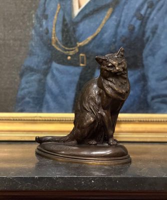 une statue représentant un chat assis sur une table, à côté d'un tableau