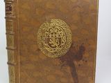 an old book with a gold design on it sitting on a white surface