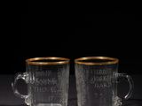 two clear glass cups with gold rims on a black surface